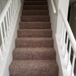 A staircase with brown carpet and white railing.