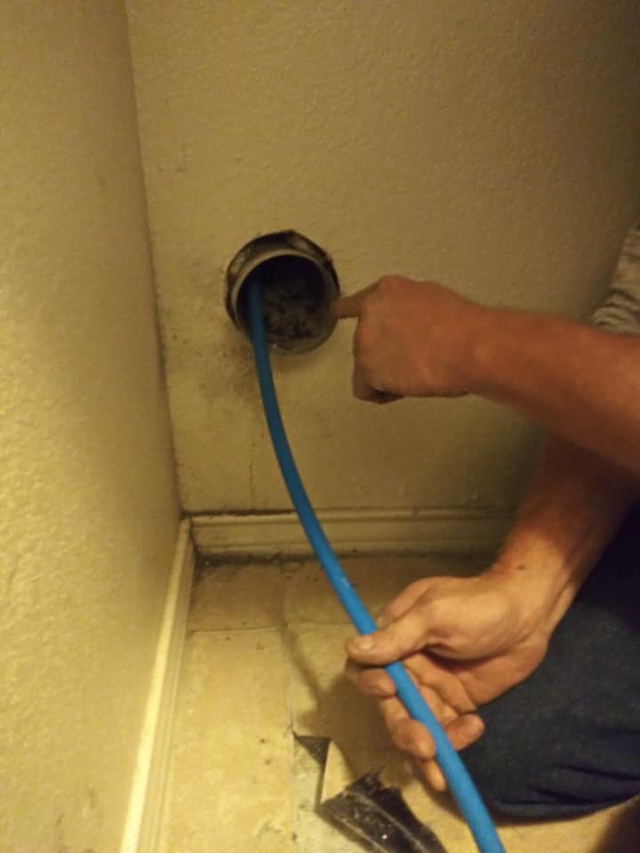 A person is holding a blue hose in the corner of a bathroom.