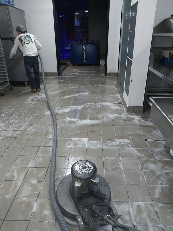 A man is cleaning the floor of an industrial kitchen.