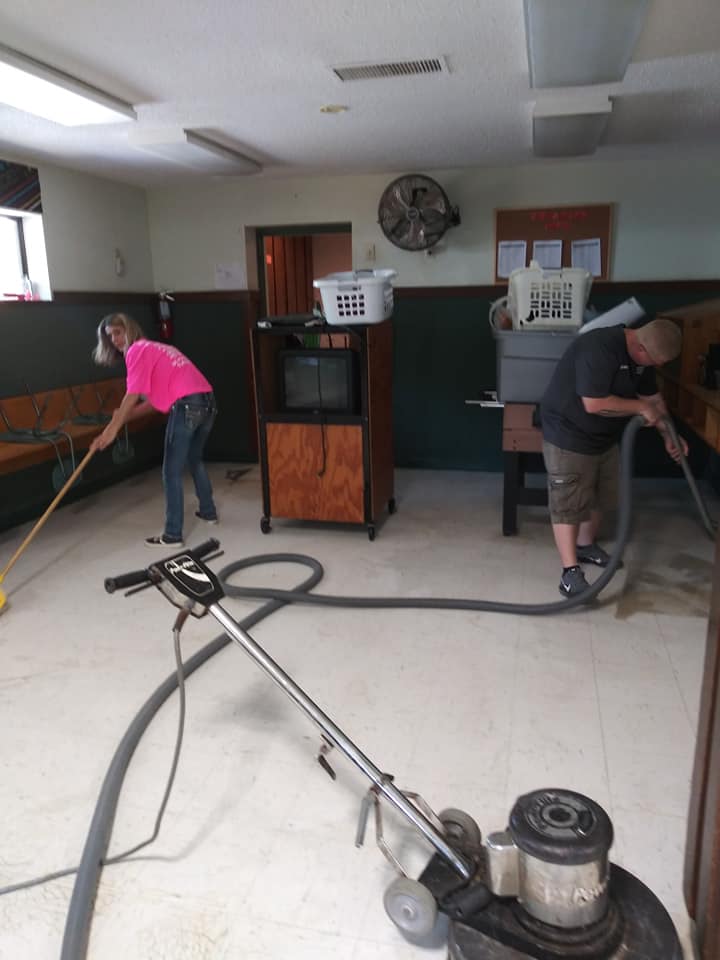 Two people cleaning a room with vacuum and hose.