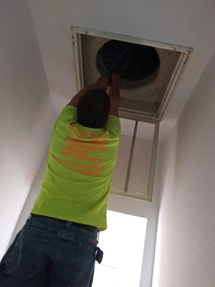 A man in an orange shirt is fixing the air vent.